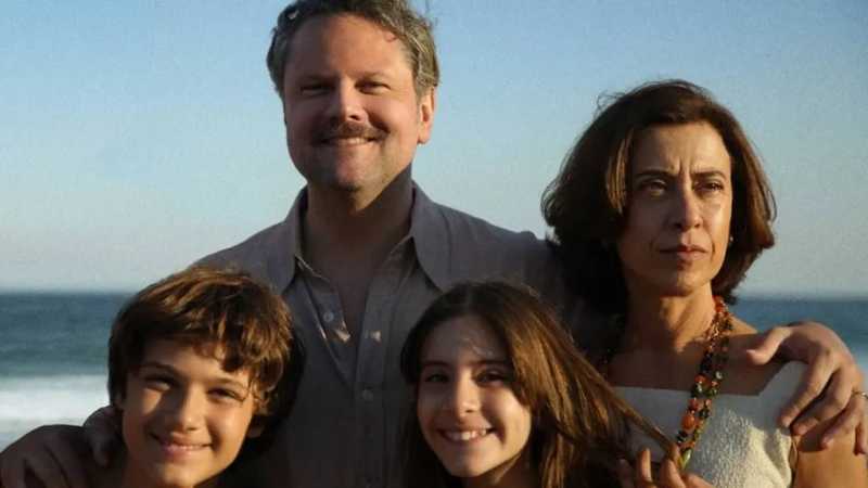 Homem e mulher abraçam dois jovens sorridentes diante do mar sob a luz do fim de tarde