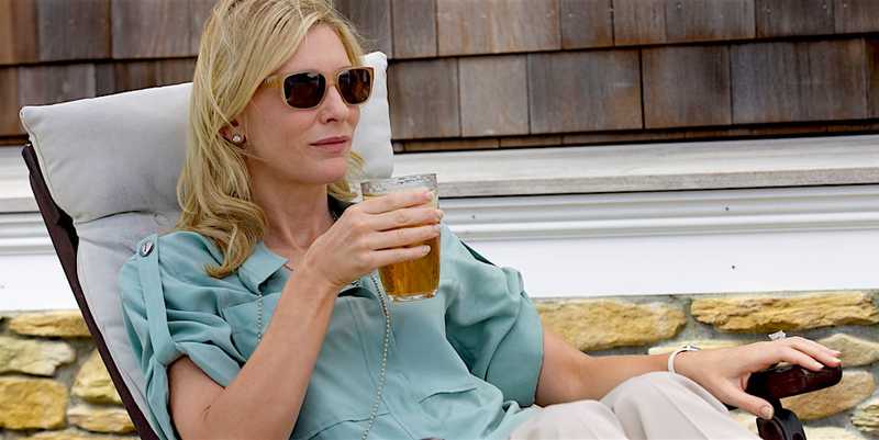 Cate Blanchett como Jasmine, de óculos escuros, segurando um copo numa espreguiçadeira