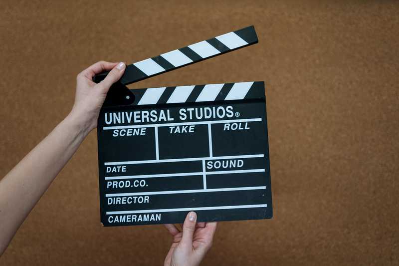 Mãos segurando uma claquete de cinema sobre um fundo marrom