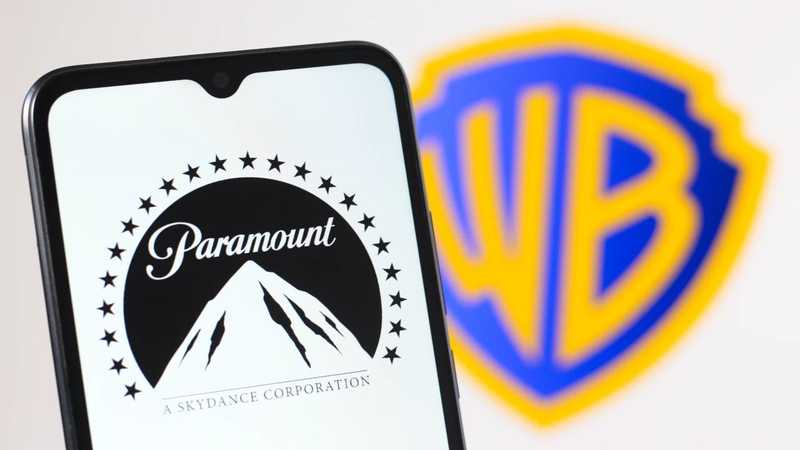 Celular exibindo o logo da Paramount Skydance em frente ao escudo azul e amarelo da Warner Bros.