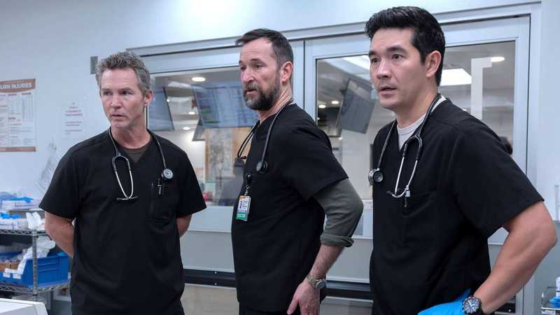 Três médicos de avental preto com estetoscópio observam algo fora do quadro no pronto-socorro da série The Pitt