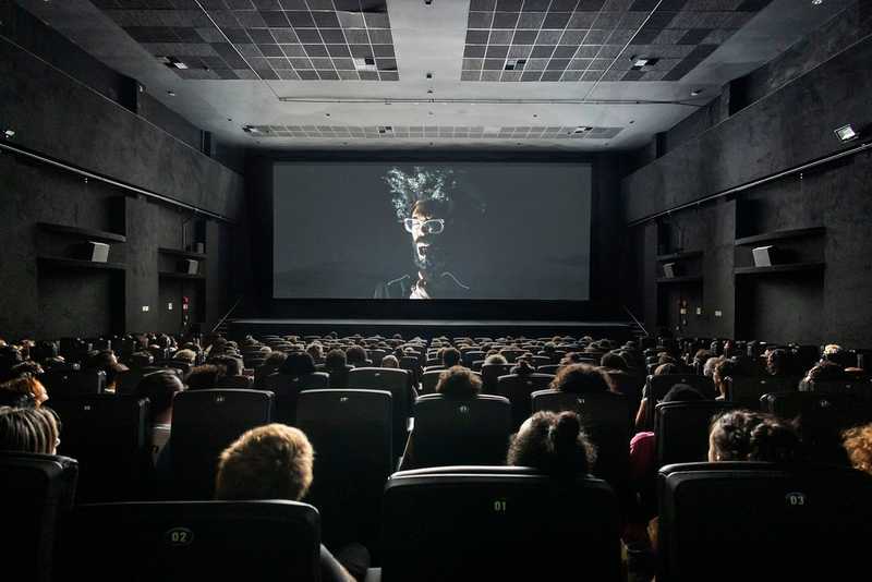 Plateia em sala de cinema durante sessão da Mostra de São Paulo, com close em preto e branco projetado na tela
