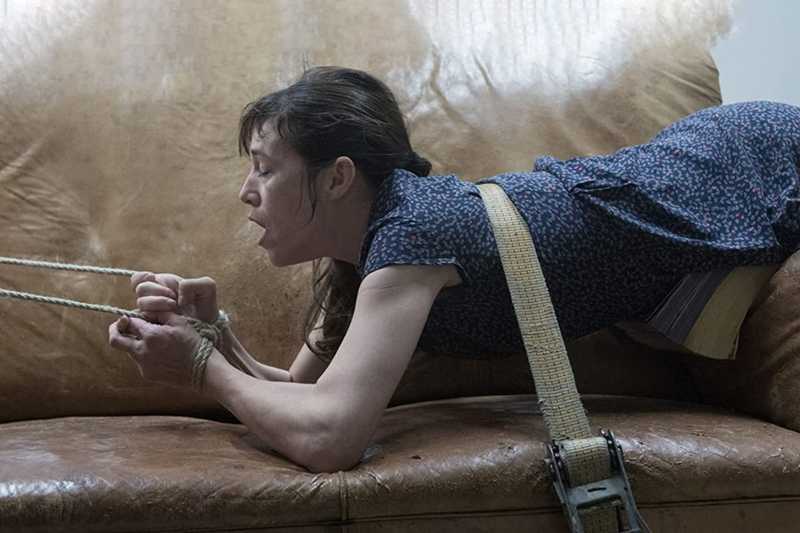 Charlotte Gainsbourg, como Joe, presa por uma cinta e cordas num sofá de couro, com expressão de dor e esforço