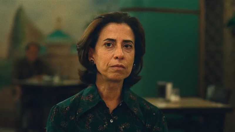 Fernanda Torres como Eunice Paiva, de camisa verde estampada, sentada num restaurante em cena de Ainda Estou Aqui