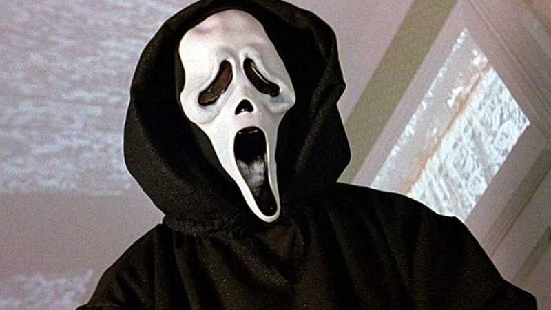 O assassino mascarado Ghostface com a máscara branca e capa preta em cena do filme Pânico