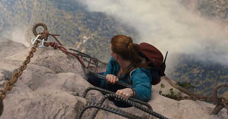 Alpinista de cabelos ruivos se agarra a correntes e barras de ferro numa rocha com abismo ao fundo em cena de A Queda 2: No Limite